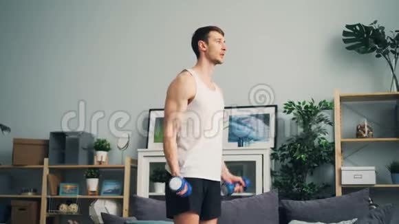 强壮的年轻人在家里用哑铃锻炼手臂和肩膀视频的预览图