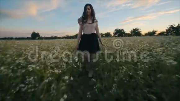 美丽的年轻黑发女孩一头波浪状的头发穿着黑色的裙子在花田里奔跑后景慢动作视频的预览图