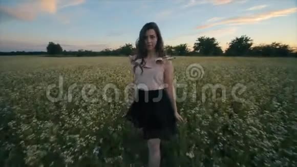 美丽的年轻黑发女孩一头波浪状的头发穿着黑色的裙子在花田里奔跑后景慢动作视频的预览图