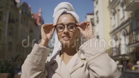 一幅年轻女子戴着毛巾戴着眼镜站在街上微笑着看着相机的肖像自信视频的预览图