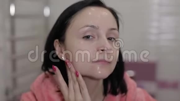 年轻的白种女人在脸上涂面霜家庭面部spa程序视频的预览图