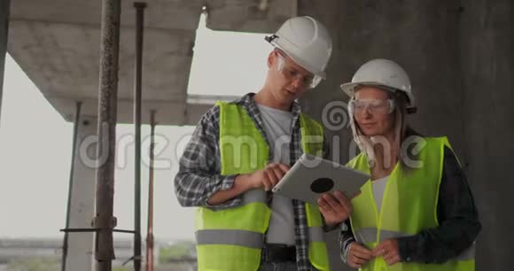 专业工程师穿着安全背心和头盔工作与数字平板和蓝图视频的预览图