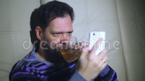 一个留着胡子的男人在智能手机上屏幕上看新闻喝茶响应电话从一个惊喜视频的预览图
