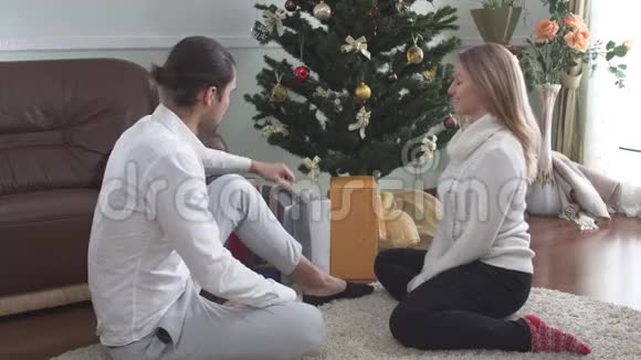 漂亮的男人把圣诞礼物送给坐在地板上的妻子漂亮的女孩惊喜又快乐视频的预览图