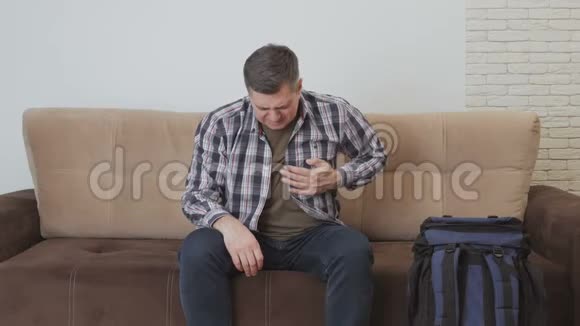 一个中年男子坐在沙发上手握在心脏区域感觉到剧烈的疼痛视频的预览图