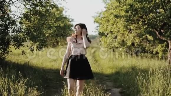 美丽的年轻女子穿着黑色的裙子波浪般的头发走在森林里的小径上微笑着旋转视频的预览图