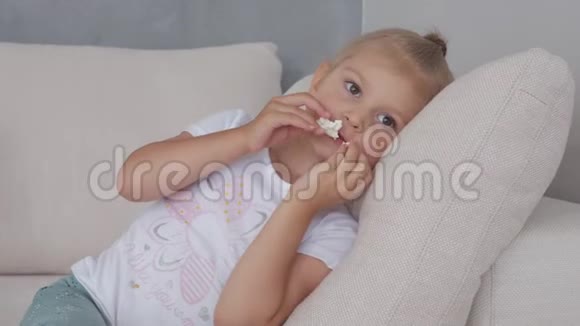 一个小女孩在软榻上吃着爆米花看着电视屏幕视频的预览图
