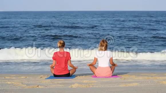 年轻女性在日落时坐在平静的海滩上的莲花姿势练习瑜伽视频的预览图