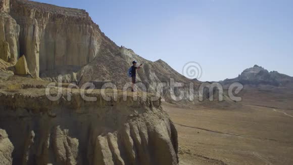 一位年轻的旅行者站在悬崖边上在智能手机上拍照视频的预览图