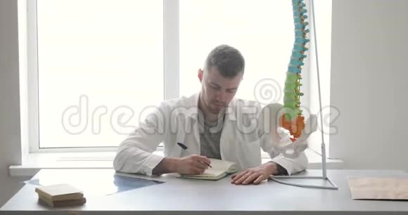 骨科医生正坐在办公室里做文书工作桌上摆着脊柱模型视频的预览图