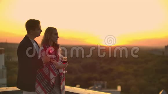 年轻的已婚夫妇在屋顶上拥抱并喝着戴着格子花格子的酒杯中的红酒欣赏着视频的预览图