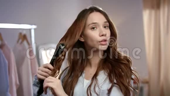 漂亮的女人用铁造型头发布鲁内特女孩在早上烫头发视频的预览图