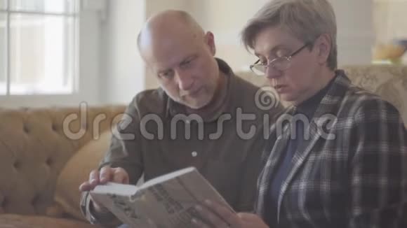 年长的夫妇男人和女人坐在沙发上拿着一本书互相交谈和微笑家庭关系视频的预览图