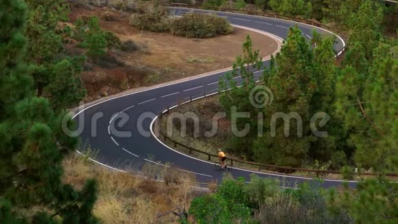 一个穿着黄色T恤的男子骑着自行车在高山上的公路上视频的预览图