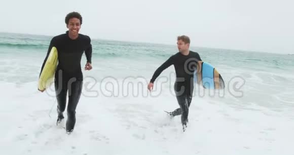 两名男性冲浪者在海滩上与冲浪板一起奔跑的正面景色视频的预览图