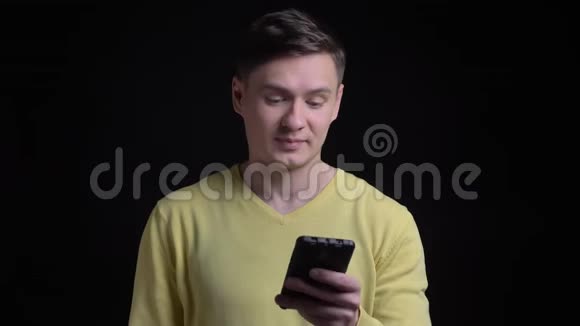 穿着黄色毛衣的中年白种人在黑色背景下的智能手机上愉快地在视频聊天的肖像视频的预览图