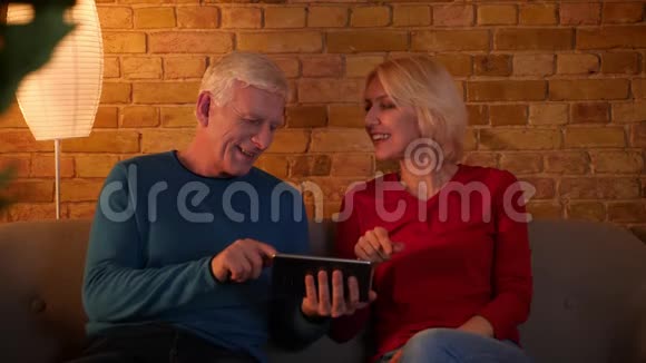 高年级幸福夫妇使用平板电脑的特写镜头幸福地坐在舒适的室内沙发上微笑视频的预览图