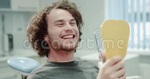 有魅力的牙医病人坐在蓝色的牙医椅上拿着一面镜子看着他在一一次视频的预览图