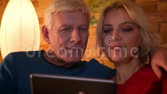 一对老年幸福夫妇的特写镜头他们用平板电脑坐在沙发上在舒适的公寓里休息视频的预览图