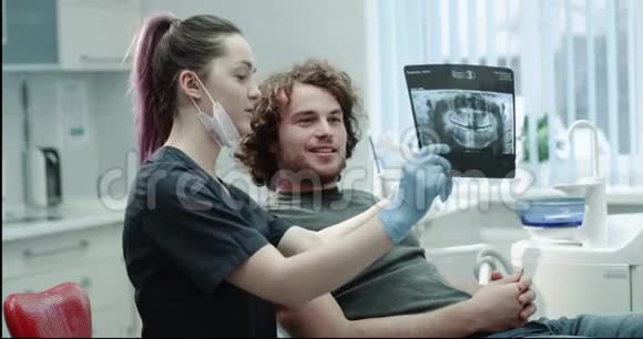快乐的牙医病人与他的医生友好交谈牙医向病人展示他的结果视频的预览图