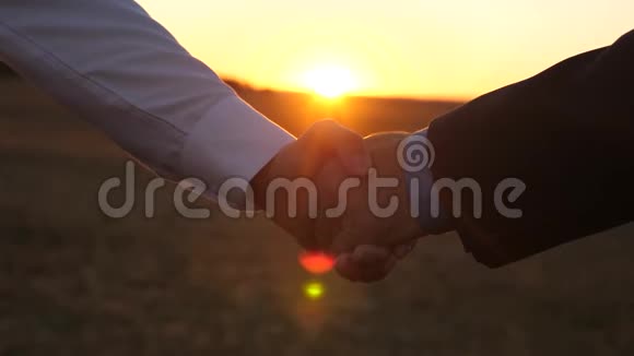 日落时握手一个穿着蓝色衬衫和夹克的男人和一个穿着白色衬衫的男人在夕阳下在美丽的阳光下握手视频的预览图