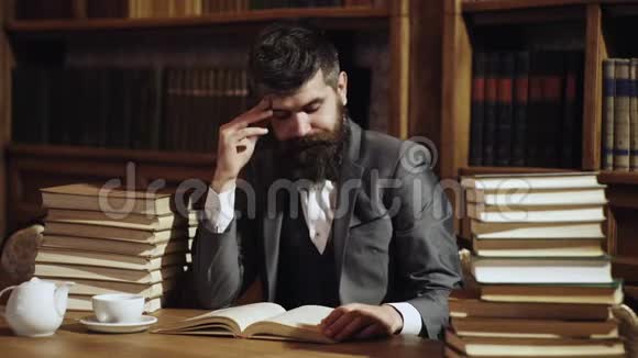 穿着经典西装的人忙碌的教授坐在书堆旁的图书馆里书架上放着书视频的预览图