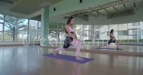 漂亮的黑发女人在明亮的健身房里用玻璃墙在垫子上做锻炼视频的预览图