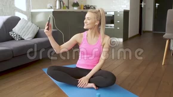 年轻迷人的运动女性坐在瑜伽垫上用手机自拍视频的预览图