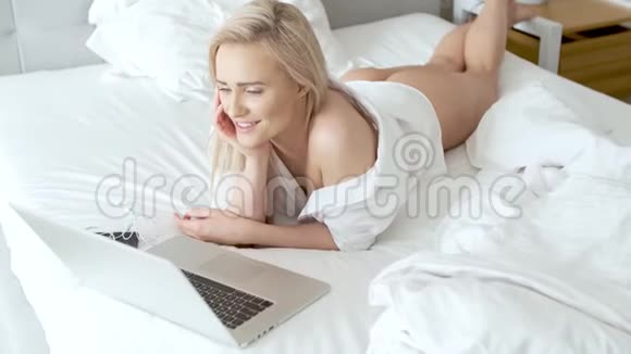 一个微笑的金发女人躺在笔记本电脑前的床上视频的预览图