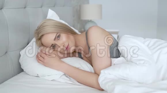在明亮的卧室里躺在床上的一个性感的金发女郎视频的预览图