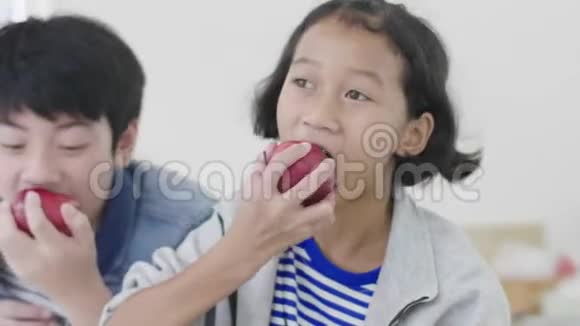 年轻的亚洲男孩和小女孩吃苹果微笑着看镜头的肖像视频的预览图