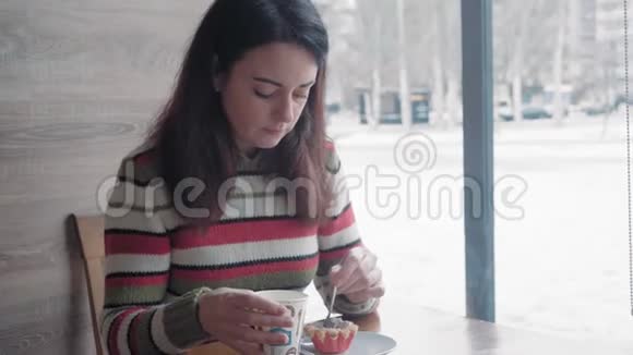 近景漂亮的女人在冬天的咖啡馆里吃蛋糕在窗外体贴地看着视频的预览图