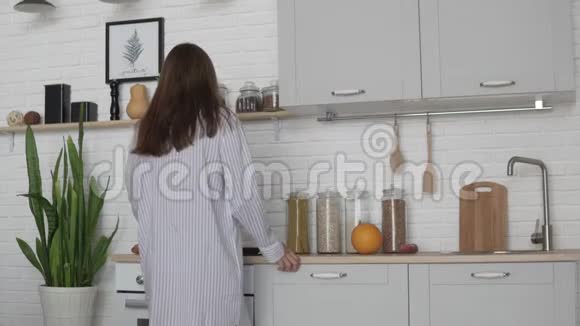 小睡衣的年轻女子早上在厨房准备早餐视频的预览图