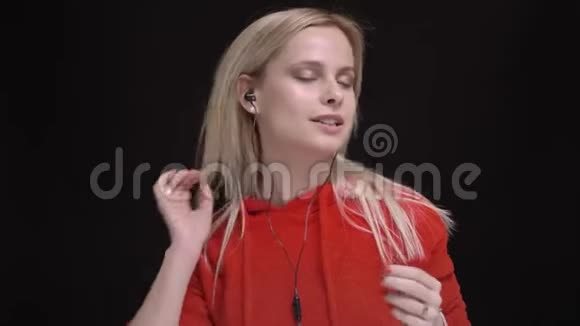 白毛白种人年轻女孩穿着红色毛衣听着耳机里的音乐和在黑色上唱歌的肖像视频的预览图