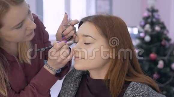 专业化妆师女孩在客户4K的眼皮上做阴影的阴影视频的预览图