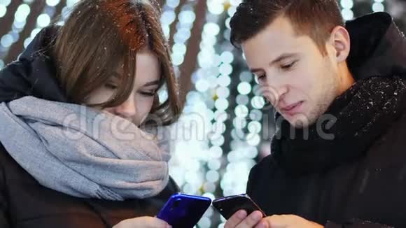 在下雪的夜晚圣诞节和新年里美丽的一对夫妇使用移动应用程序视频的预览图
