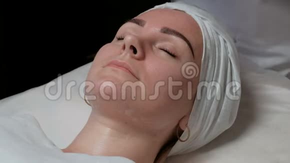 一个年轻的女人躺在一个医疗美容院的皮肤清洁过程中闭着眼睛宇宙学家他的手视频的预览图
