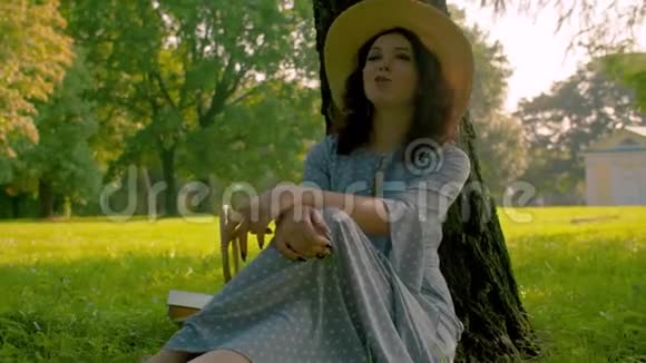 诗意的美丽女孩坐在松树附近的公园里视频的预览图