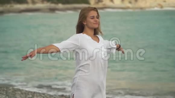 年轻漂亮的女孩站在海边张开双臂微笑着在夏天休息的时候加入海风视频的预览图
