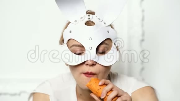 白色背景上戴皮面具的性感女孩关闭复活节兔子女孩吃胡萝卜隔离在白色背景视频的预览图