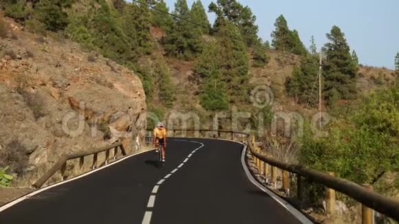 一个穿着黄色T恤的男子骑着自行车在高山上的公路上视频的预览图