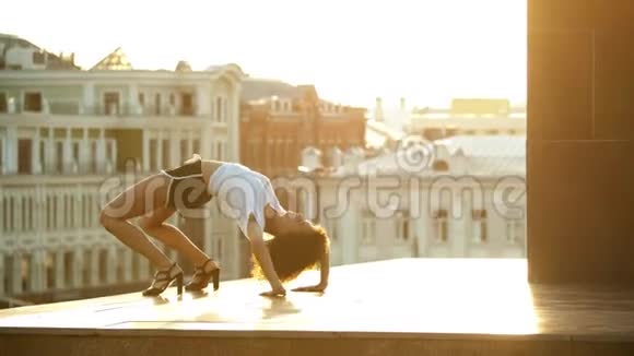 一个年轻迷人的女人卷发在地上表演舞蹈元素建筑物的背景日落视频的预览图