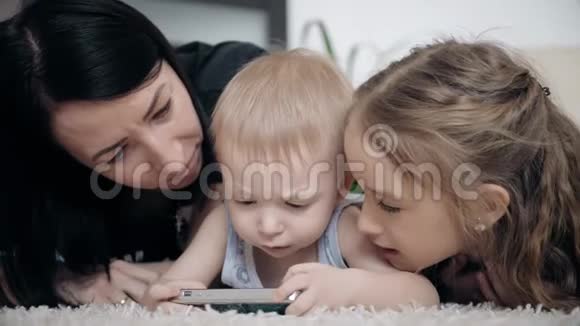 年轻的母亲和两个孩子在家里的地板上玩平板电脑生活方式视频的预览图