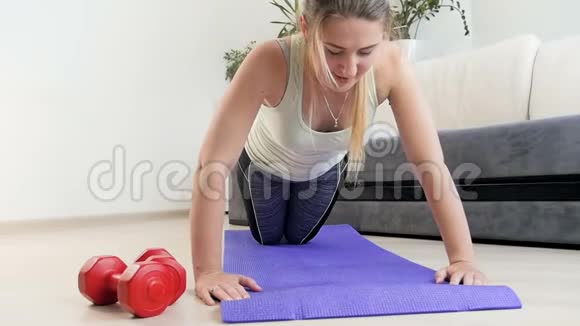 疲惫的年轻女子在家中的健身垫上做俯卧撑后摔倒在地板上的慢动作镜头视频的预览图