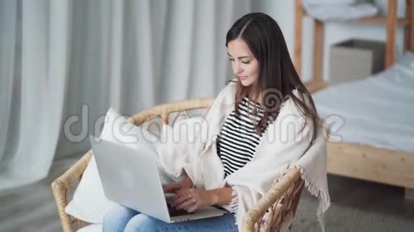 漂亮的年轻女人坐在扶手椅上用笔记本电脑自由职业者在家工作视频的预览图
