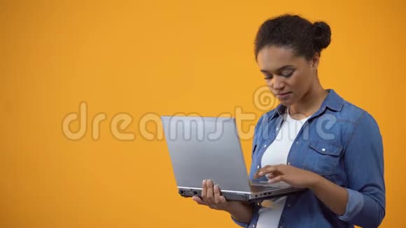 漂亮的非裔美国妇女在笔记本电脑上打字单独的黄色背景视频的预览图