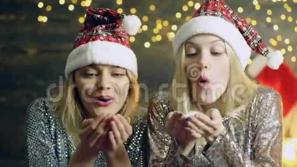 戴着新年帽的女孩们在吹手上的雪从手上吹雪新年心情的概念迷人的冬天视频的预览图