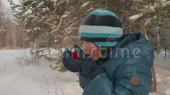 性格开朗的少年在雪林中喝热茶冬天散步视频的预览图