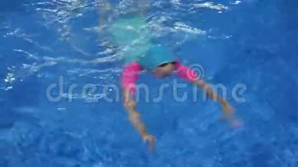 穿着泳衣帽子和护目镜的小女孩正在潜水和游泳到游泳池视频的预览图