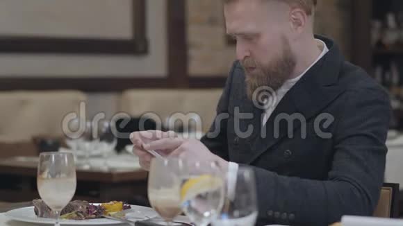 肖像自信的金发碧眼男子穿着时尚夹克拿着手机坐在一个现代化的房间里拍照视频的预览图